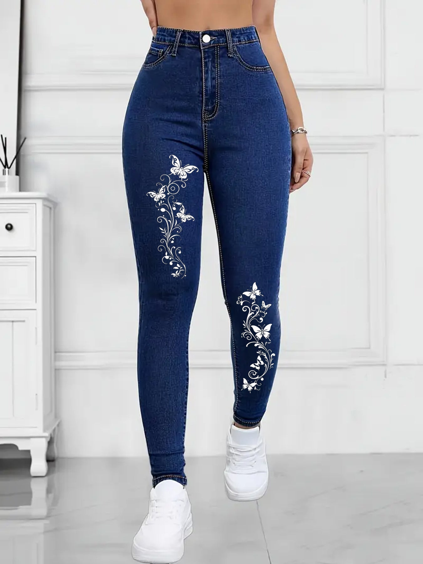 Blue jeans with butterfly patterns worn by a person in a minimalistic setting.